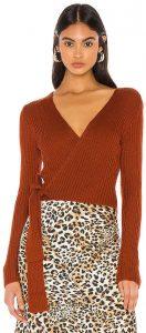 A woman wearing a burnt orange wrap sweater with a leopard print skirt.