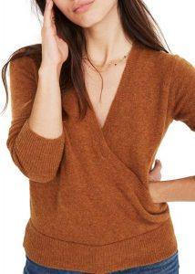 A posing woman wearing an orange faux wrap pullover sweater.