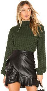 A woman wearing a dark green knit sweater tucked into a leather skirt.