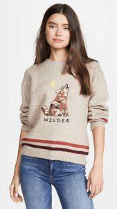 A woman wearing a graphic pullover sweater that features a howling wolf and the word ‘wilder’.